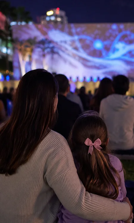 Family Watching SoundScape Park Event Mother and young daughter watching a nighttime outdoor projection event at SoundScape Park