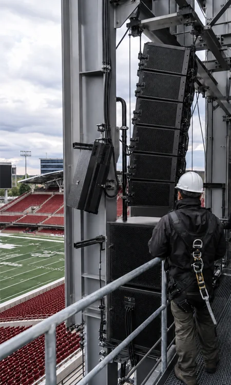 Stadium Speaker Array Integration Technicians inspecting an integrated stadium loudspeaker array mounted near a scoreboard structure.